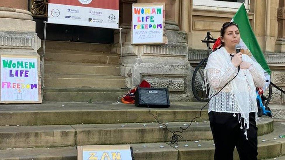 A woman speaks at a vigil for Iran held in Ipswich. There are signs behind her that read women, Life, Freedom.