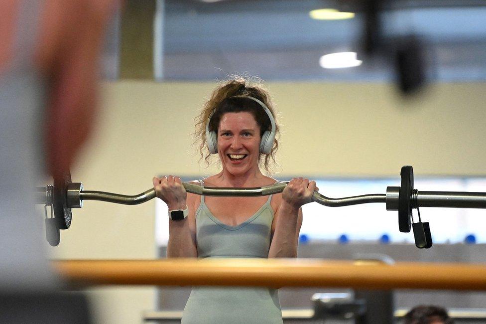 A woman lifts a weight whilst smiling at herself in the mirror