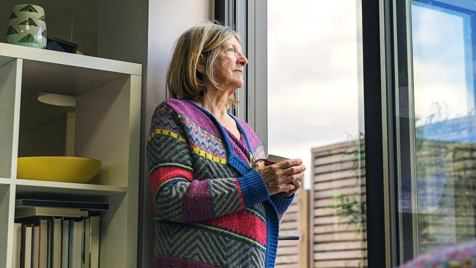 A senior woman looking through a window in her home on a wet day