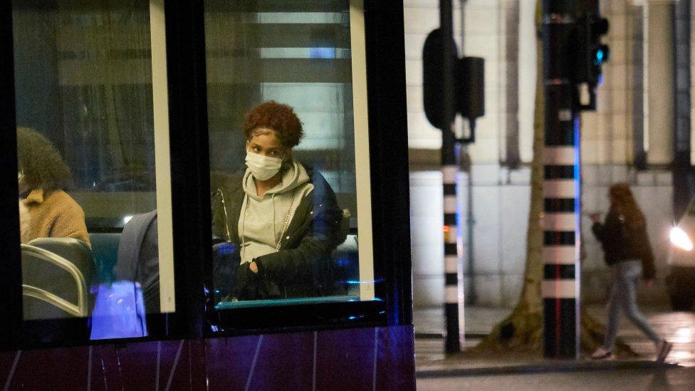 A woman in the Netherlands sits on a tram while wearing a mask