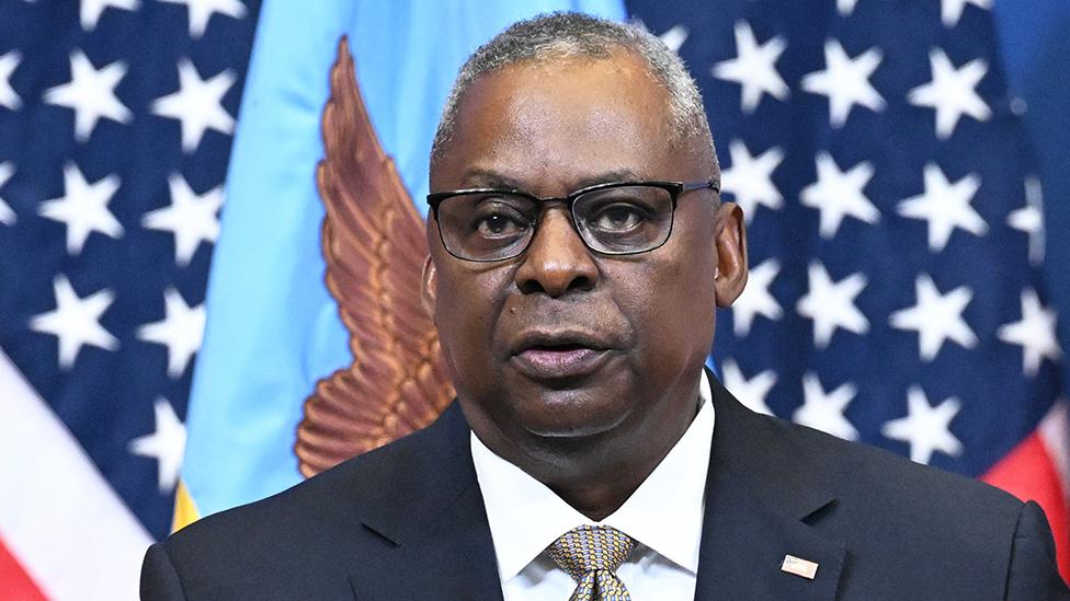 US Secretary of Defense Lloyd Austin dressed in a suit and wearing glasses in front of the US and Department of Defense flags in Brussels on 11 October