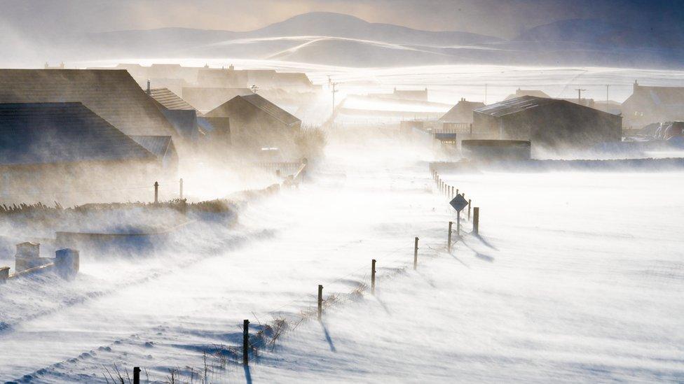 A wintry scene in Orkney with wind blowing snow across a road