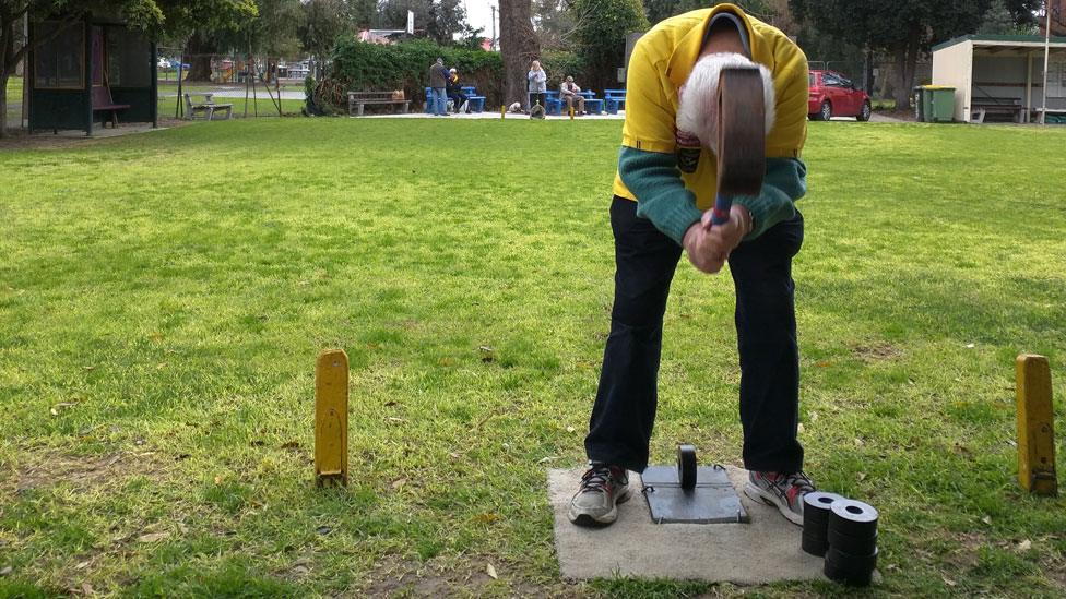 Facing backwards, John McMahon raises a mallet as he prepares to hit a rubber ring between his legs