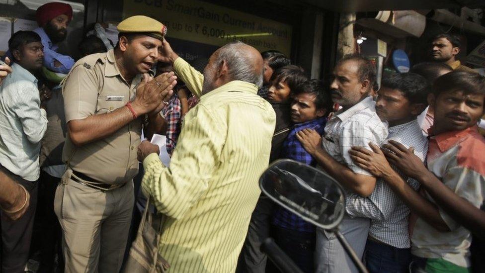 An Indian police officer pleads to an elderly man to stay in the queue as people crowd outside banks to deposit and exchange discontinued currency notes in New Delhi, India, Saturday, Nov. 12, 2016.