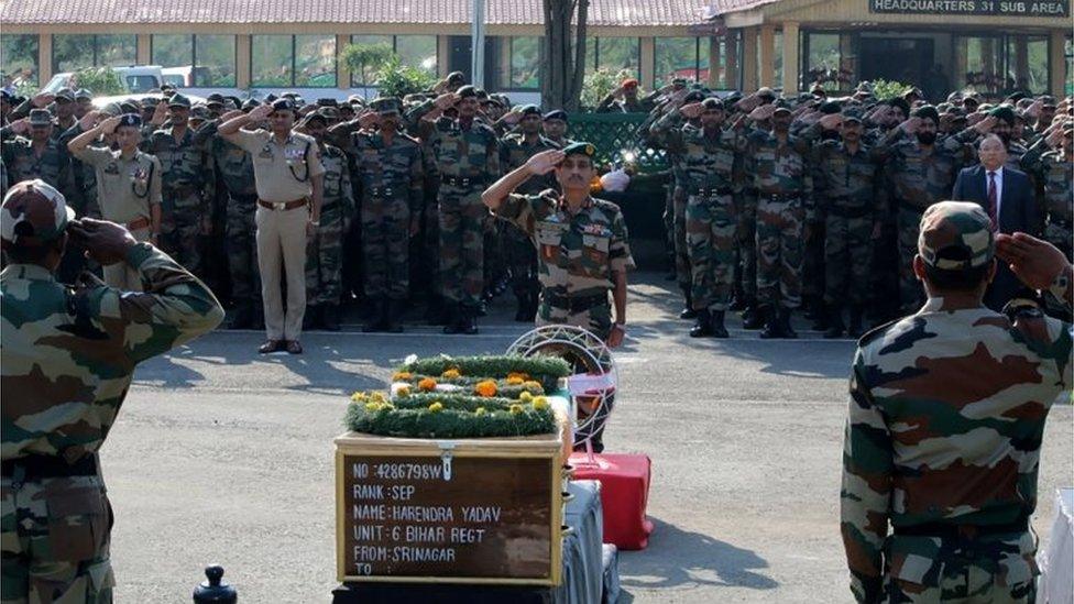 An Indian army soldier salutes the coffins of colleagues during a wreath laying ceremony for 17 Indian army soldiers killed in a gunbattle at the army headquarters in Srinagar on September 19, 2016.