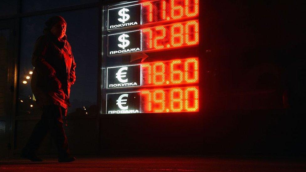 A woman walks past a board listing foreign currency rates against the Russian ruble in central Moscow