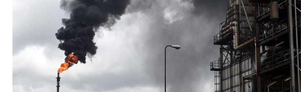 Thick black smoke billows from a pencil-thin chimney