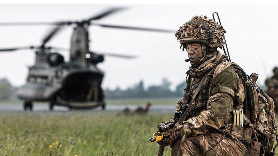 Military personnel with a gun in front of a helicopter.