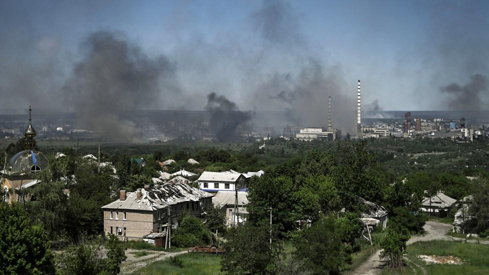 A damaged building can be seen in Lysychansk as black smoke rises from the nearby city of Severodonetsk