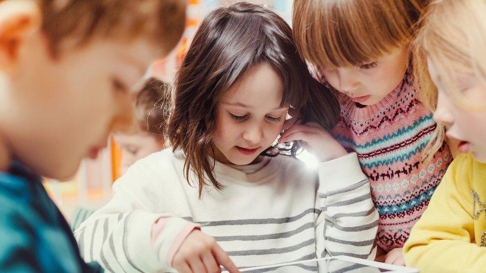 Young children gather round a tablet