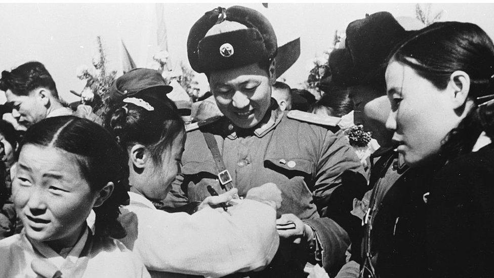 29 March 1958: Korean girls present a member of the Chinese People's Volunteer Army with a bouquet of flowers prior to the mass withdrawal of Chinese troops from North Korea