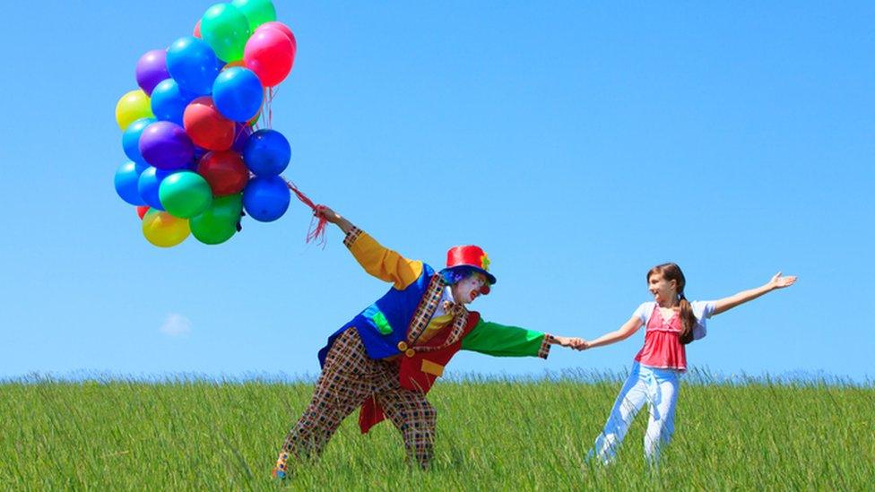 Clown holding balloons and a girls hand.