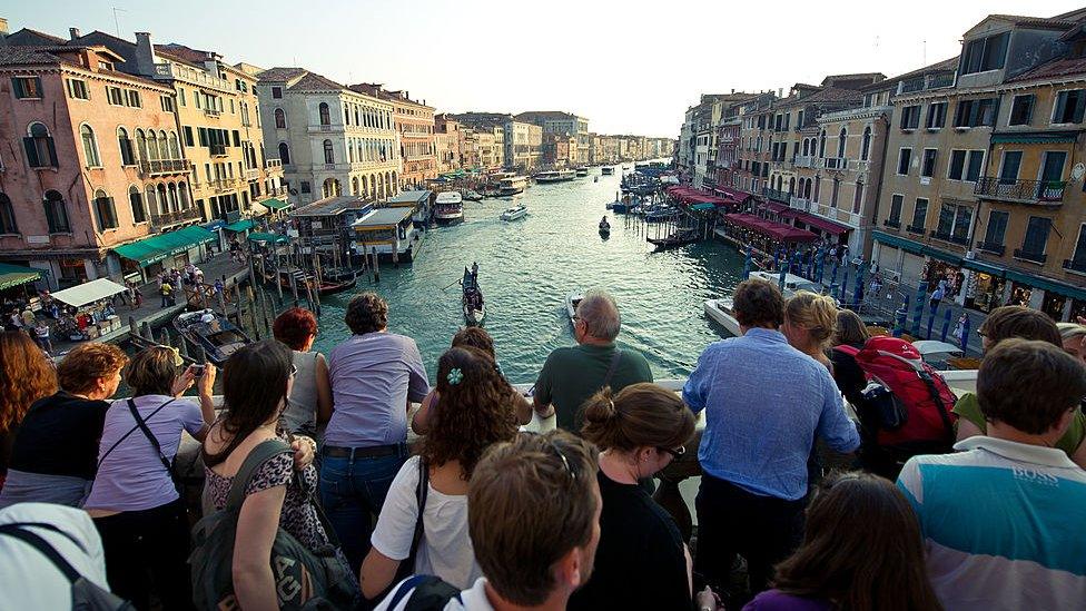 Tourists look at the view across the Grand Canal from the Rialto bridge