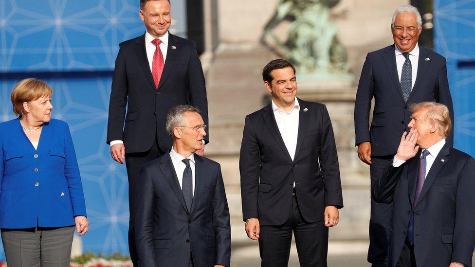 German Chancellor Angela Merkel (L) looks on as U.S. President Donald Trump speaks to other leaders as they pose for a family photo at the Park of the Cinquantenaire during the NATO Summit in Brussels,