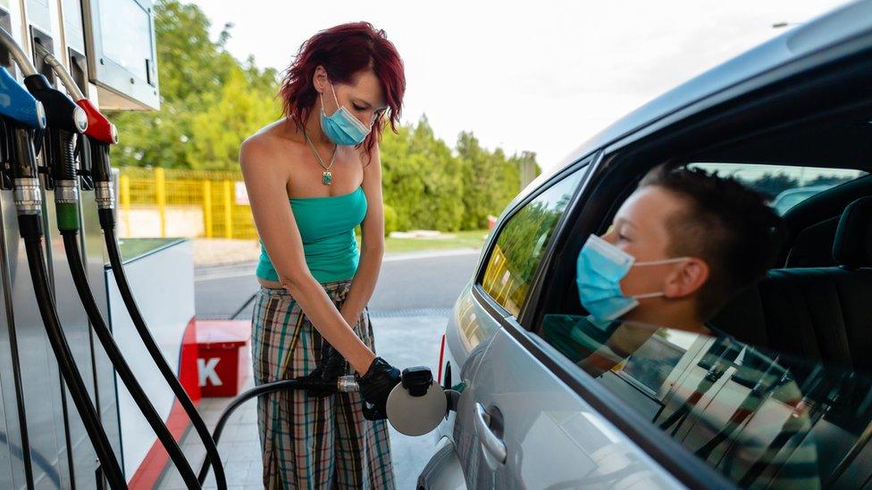 Woman filling up car with petrol with a child sitting in the car