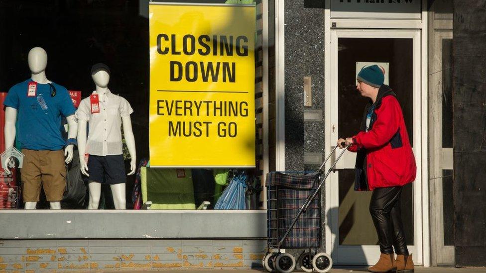 A woman pushes a shopping trolley past a clothing retailer advertising a "closing down" sale on High Row in the town centre of Darlington, north-east England in 2018