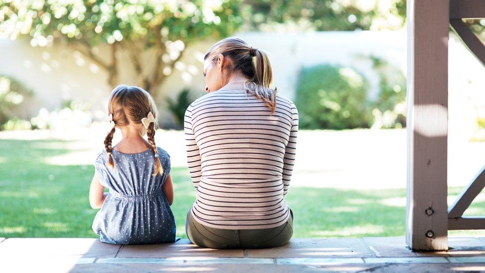 A woman and child sit together on a porch