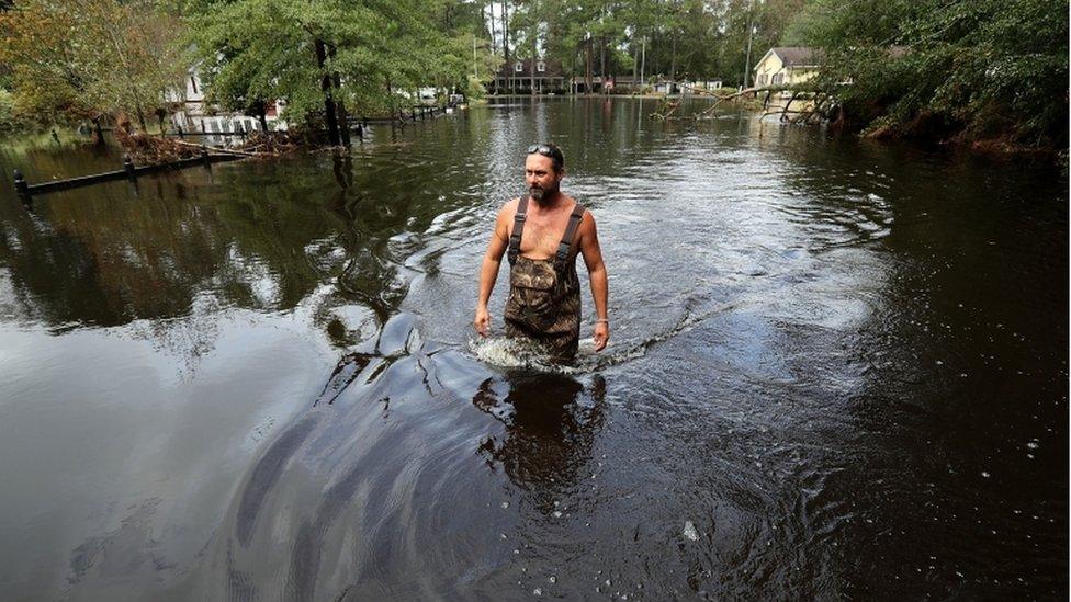 Man wades through thigh-high floodwater in neighbourhood