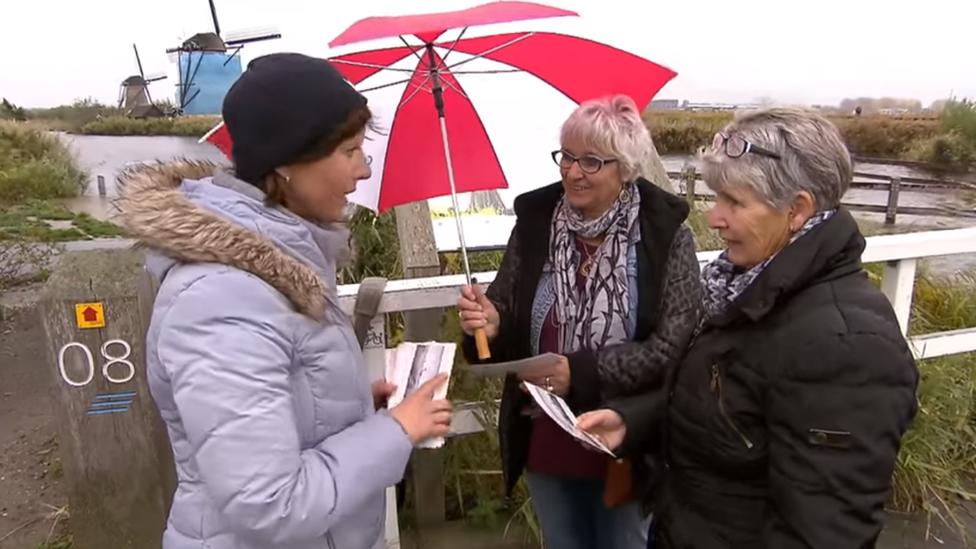 Kinderdijk inhabitant hands cards to tourists, Netherlands