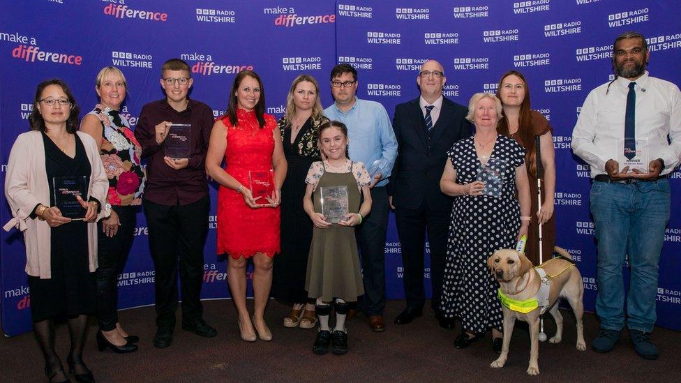 Group of people in front of purple branded banner holding glass awards.