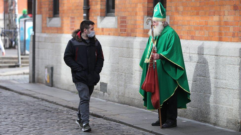 A man dressed as St Patrick watching a man with a mask walk by in Temple Bar, Dublin