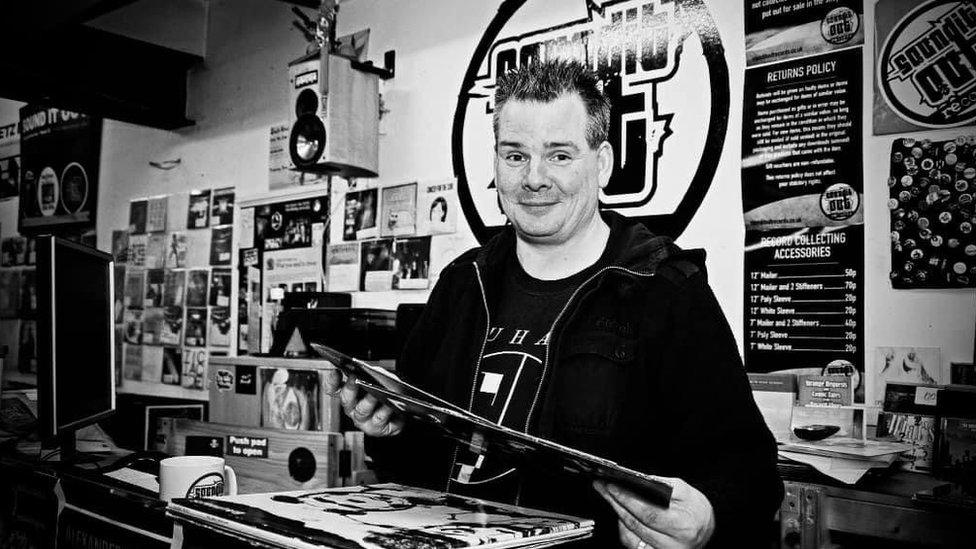 Tom Butchart, holding a vinyl record, behind the counter at Sound It Out Records