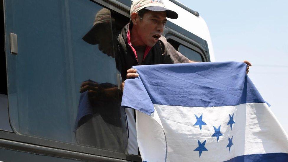 A Honduran waves a Honduran flag out of a bus window