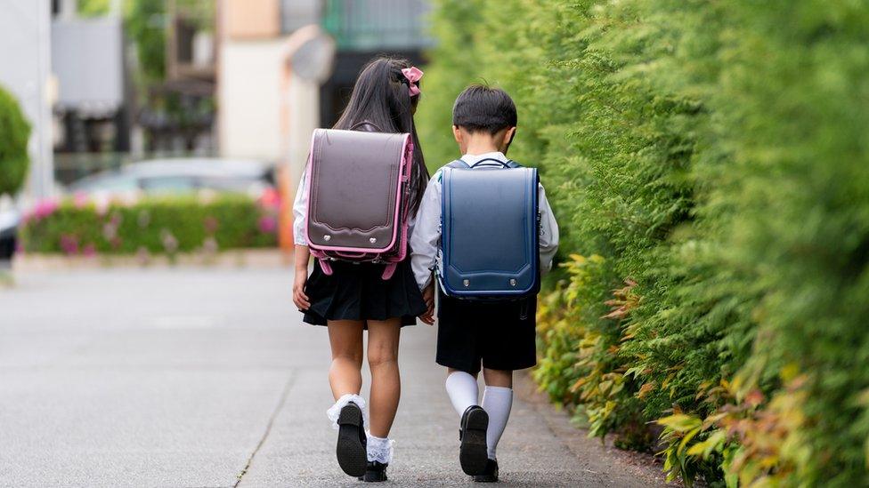 two children walking to school wearing randoseru backpacks