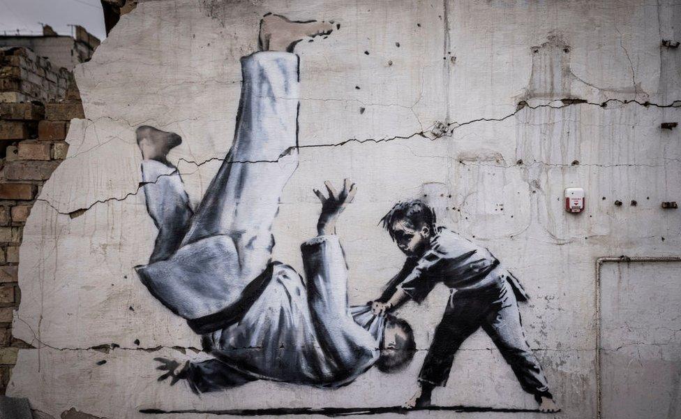 Graffiti of a child throwing a man on the floor in judo clothing is seen on a wall amid damaged buildings in Borodyanka