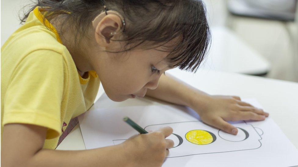 A girl with a hearing aid colouring in a picture