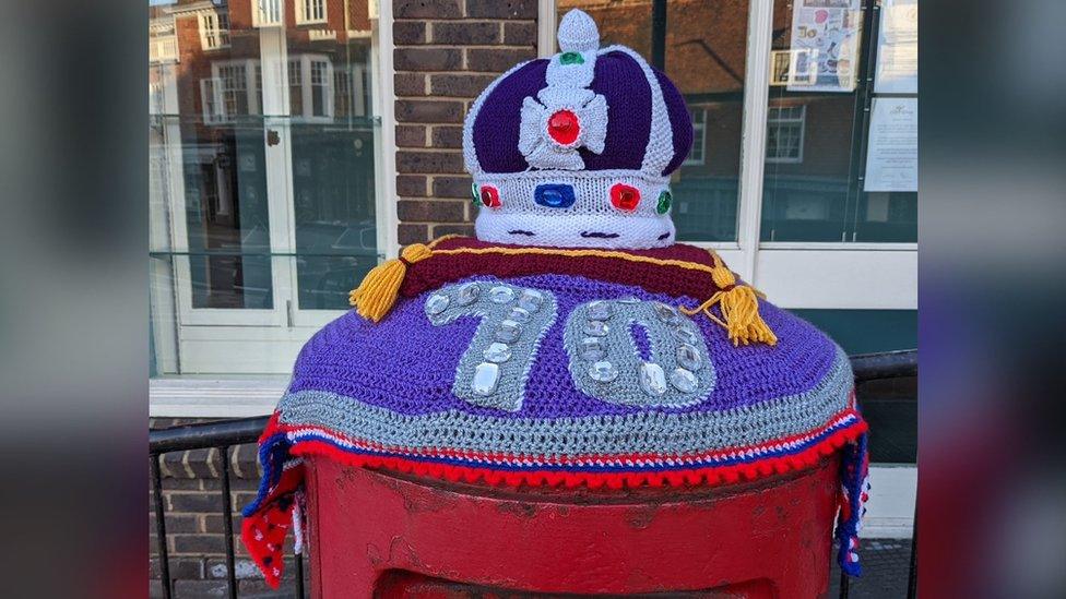 A knitted post box topper of a crown and the number 70 in Battle, East Sussex