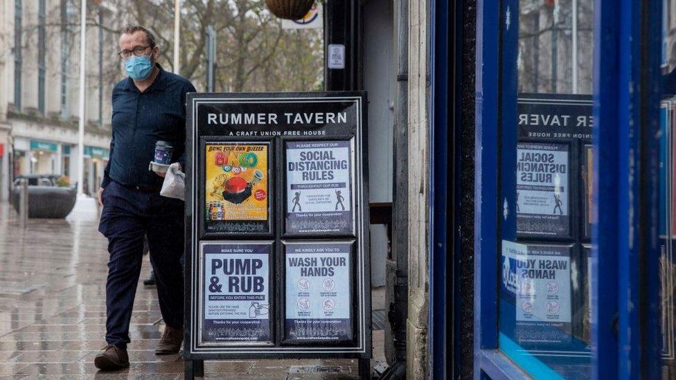 A man walks past a pub sign in Cardiff displaying social distancing notices