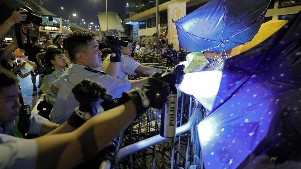 Protesters use umbrellas to block the pepper spray from police officers after clashing outside the Chinese central government's liaison office in Hong Kong