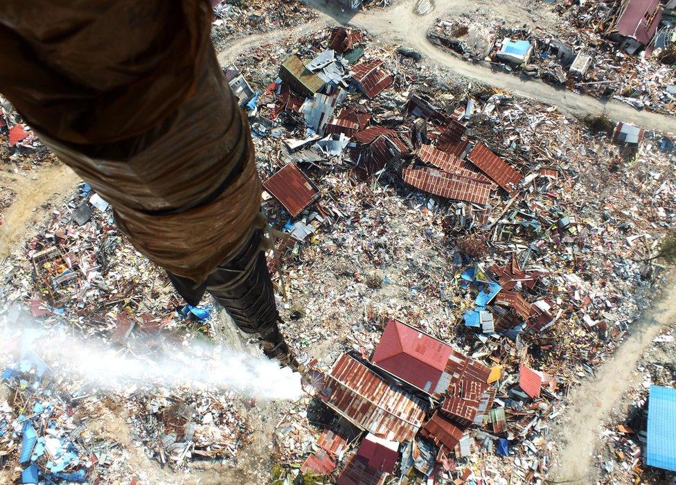 A helicopter releases disinfectant over an area affected by the earthquake in Palu, Indonesia