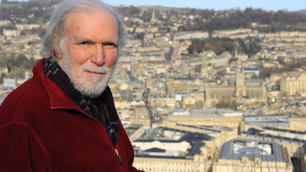 Andrew Lawrence. He is pictured to the left side of the frame and is stood with a view of the city of Bath in the distance. Andrew is facing the camera, squinting, but smiling.