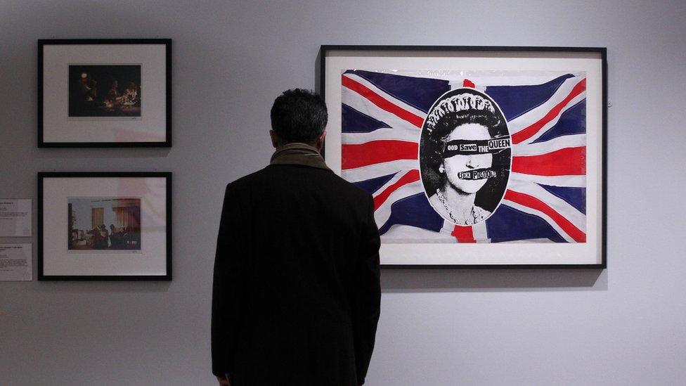 A man views a work depicting Britiain's Queen Elizabeth II entitled "God Save The Queen" (R) by artist Jamie Reid made for British punk band the Sex Pistols in 1977 during 'The Queen: Art and Image' exhibiton at the Ulster Museum in Belfast, Northern Ireland on January 14, 2012.