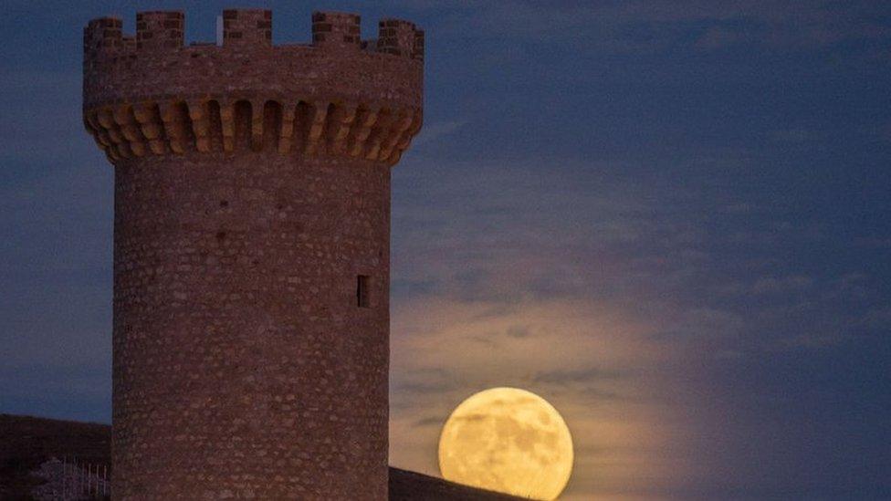 A large tower made of brick against a blue sky with the moon rising behind it