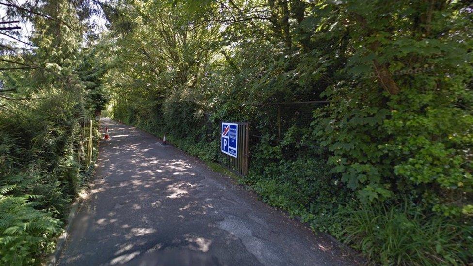 Tarmac track and gate surrounded by trees leading to Branksome Triangle site