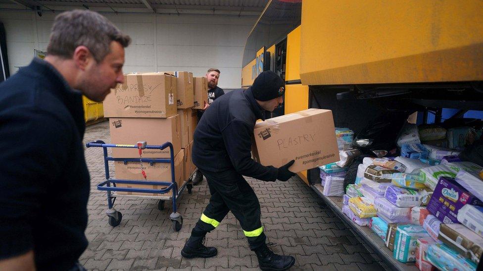 A guard loads aid supplies onto a bus in Przemysl owned by British volunteer Cliff Wilson (left) who will transport it to Ukraine