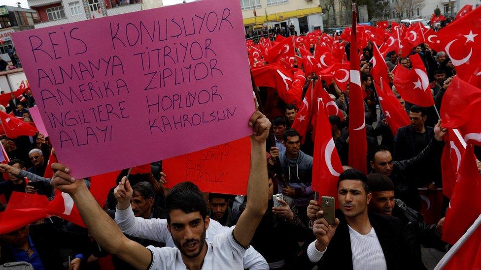 A man holds a banner during a rally which reads: "The chief (in reference to Turkey"s President Tayyip Erdogan) is speaking / Germany is trembling / America is jumping / England is quivering /Down with them all"