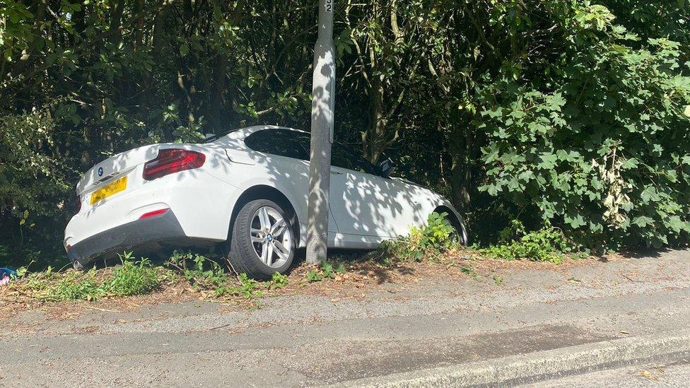 Car in bushes after coming off the road and hitting electricity poles