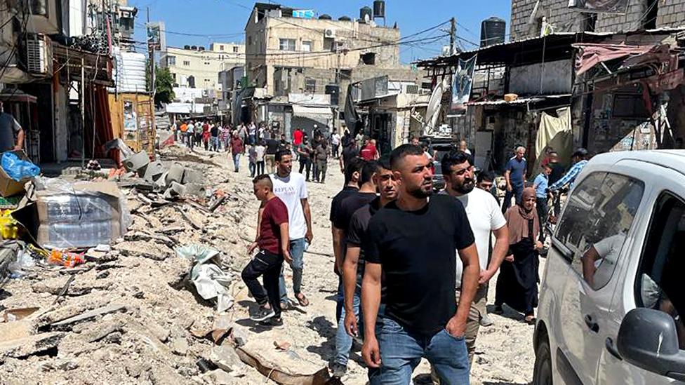 Palestinians inspect damaged vehicles, roads and vehicles in Jenin refugee camp, in the occupied West Bank, following a major Israeli military operation (5 July 2023)