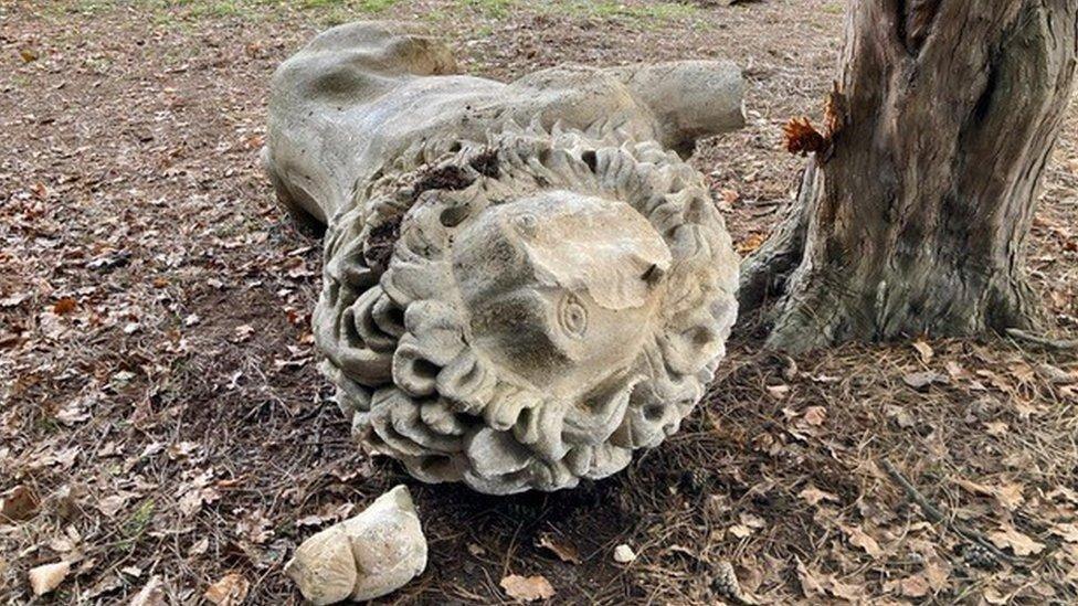 The lion sculpture after the car hit it lying on its side with its leg smashed and part of its face destroyed
