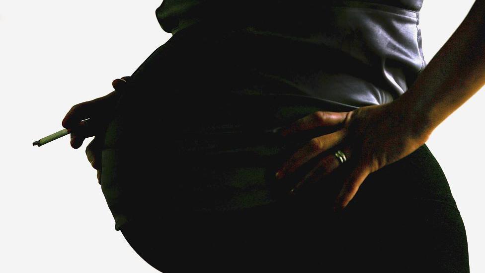 Silhoutte of a pregnant woman smoking.