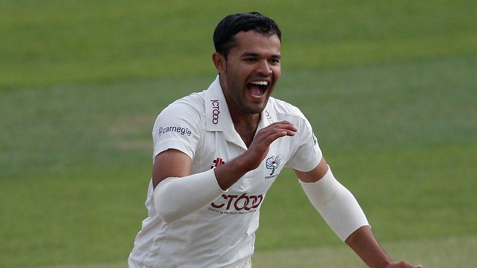 Azeem Rafiq as a young cricket player, wearing a white jersey and celebrating.