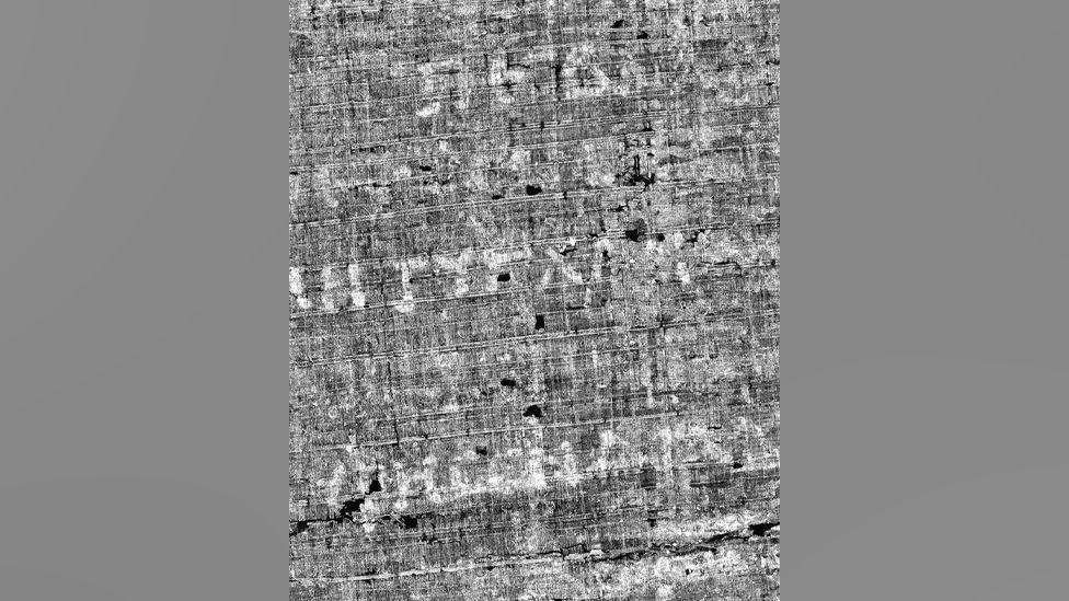 Close up view of a black and white image of an unrolled scroll from Herculaneum made by x-ray scans and AI. Some Greek letters are visible on the page - but words cannot yet be fully made out.  