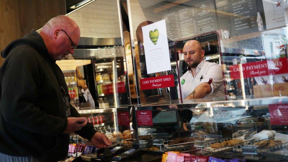 An employee is seen behind a protective screen as they serve a customer in a Pret a Manger store that has reopened for delivery and takeaway in Wimbledon on 1 May