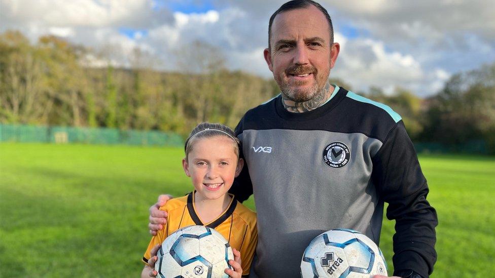 Matthew Evans with his arm around son Ollie in a field with both holding footballs