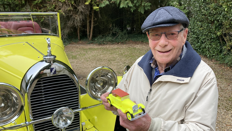 Malcolm Stern in front of his father's 1930's classic car holding a model of the car