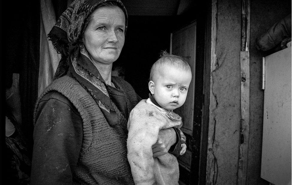 A woman holds her baby who is wearing dirty clothes